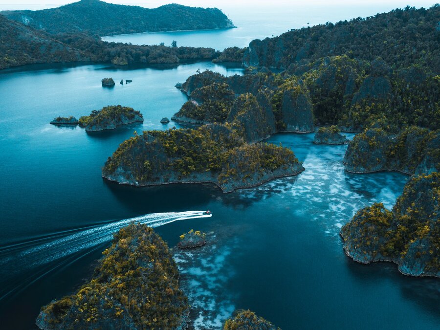 Aerial view of a speedboat weaving through Raja Ampat's limestone islands, West Papua, Indonesia